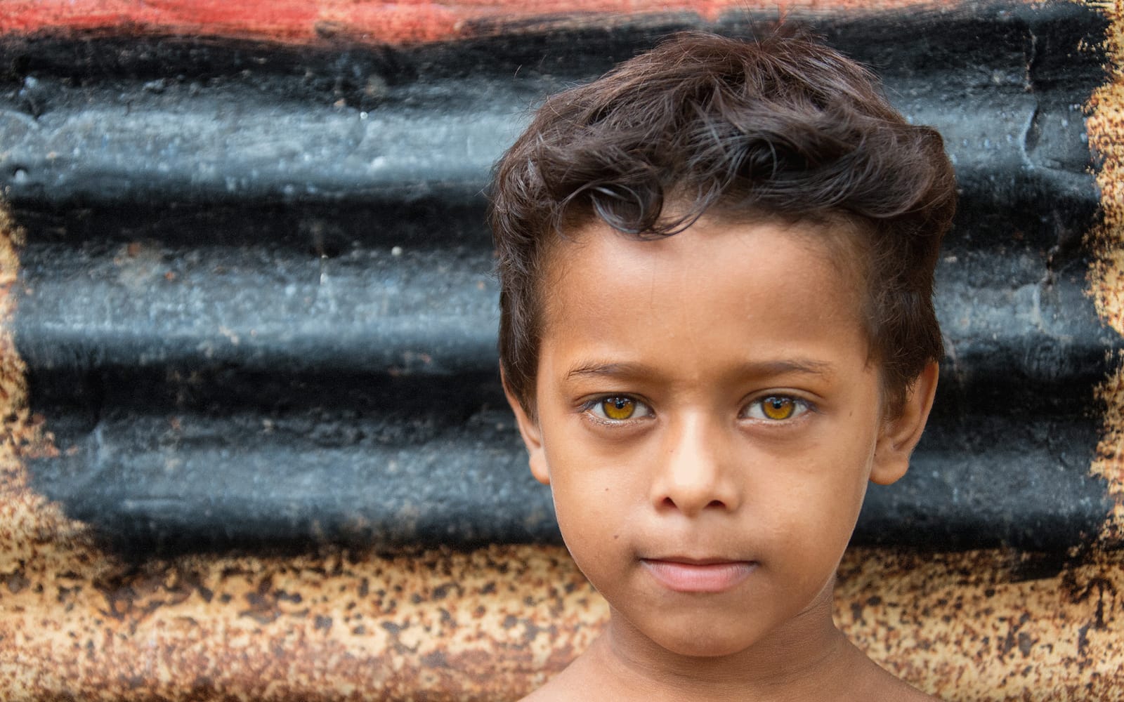 A child with mesmerizing gold eyes poses for a portrait outside of his house in Granada, Nicaragua.