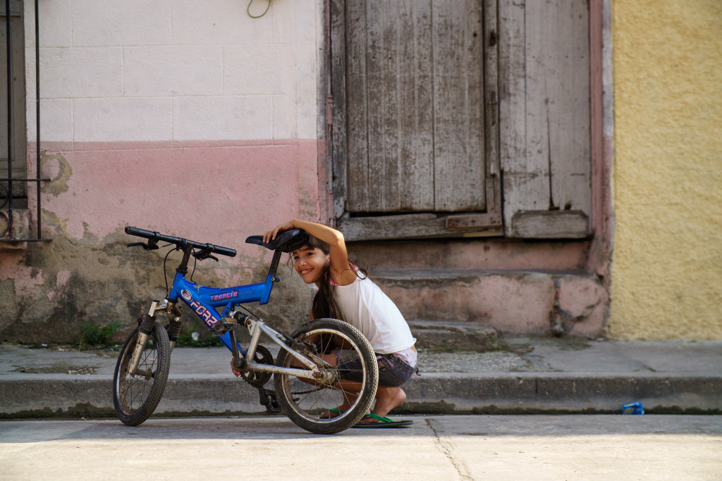 A girl fixes the chain on her bike in Holguin Cuba. She is smiling at the girls in the photo below. Photographed on a Tamron 24-70 f/2.8 at 1/640 and f/2.8