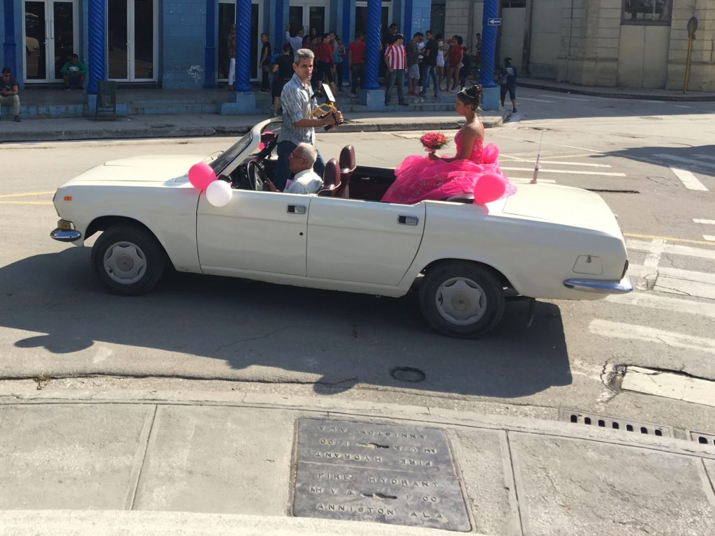 A convertible travels around the Parque Central of Holguin to celebrate the Quinceañera (15th Birthday) of a local young woman. 